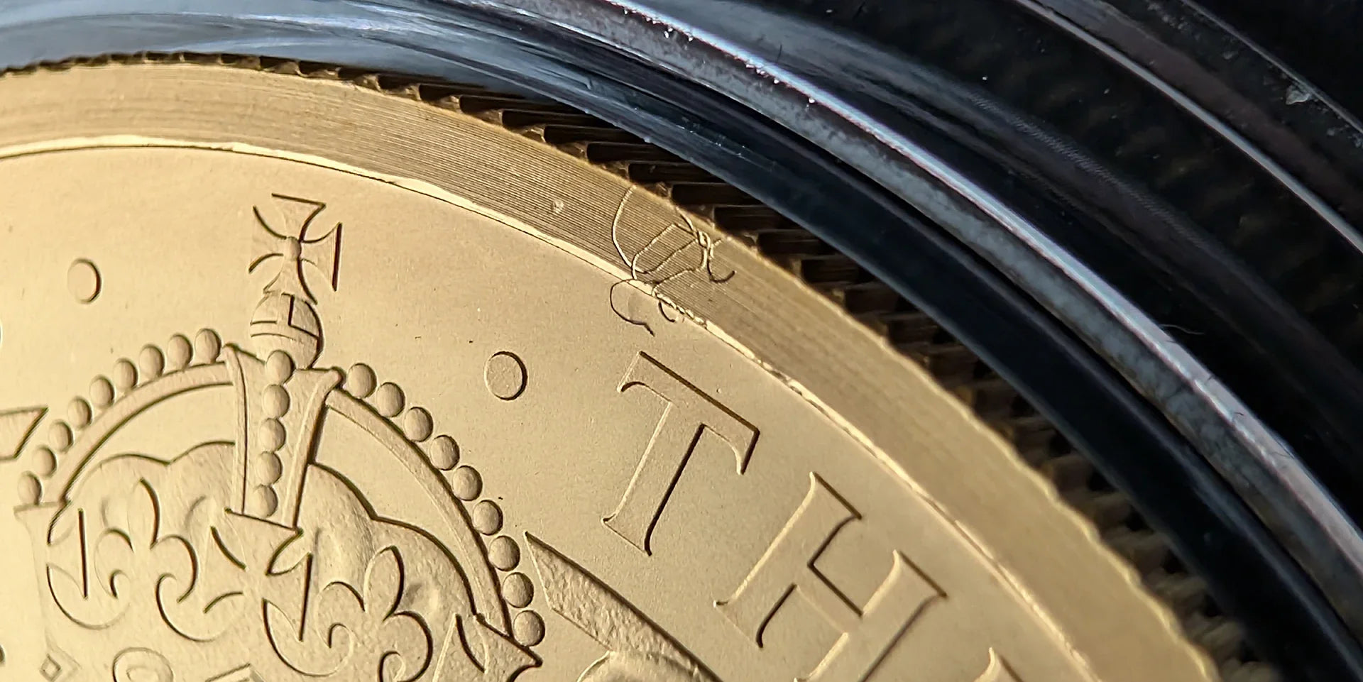 Detailed macro view of the upper rim of a gold proof coin under high magnification, capturing a trapped foreign filament and a negative die strike impression in the metal surface.